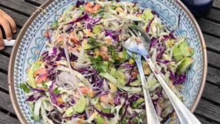 image of a salad in a white bowl with grey rims set on a wooden table outside.