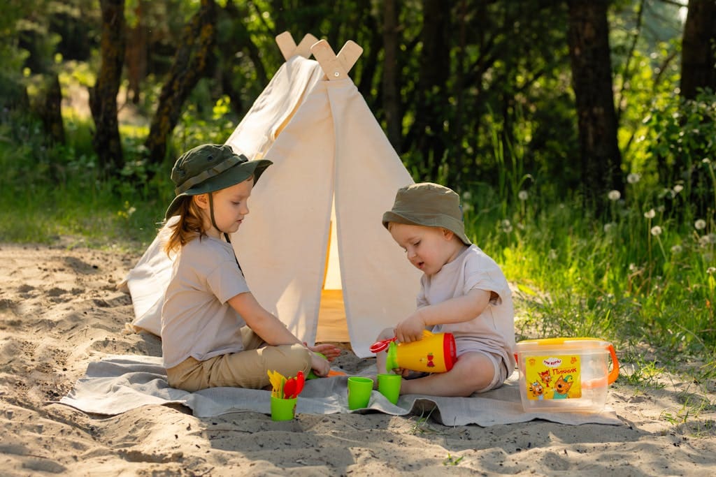 Two children enjoying summer playtime at a sandy campsite with a small tent.