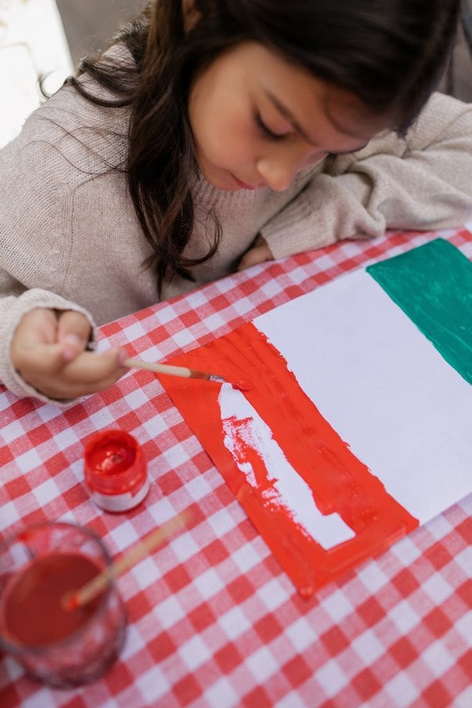 A young girl diligently paints a Mexican flag, symbolizing cultural celebration and artistic expression.